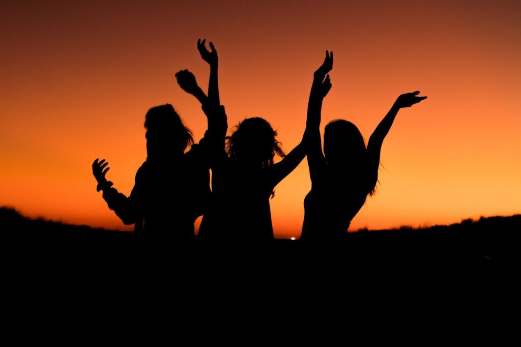 silhouettes of 3 women dancing against an orange and black background